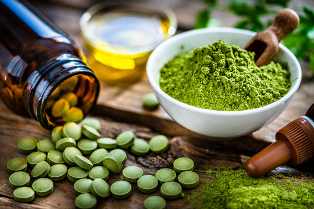 Nutritional supplement: Moringa powder in a white bowl and Moringa capsules spilling out a bottle shot on rustic wooden table. High resolution 42Mp studio digital capture taken with Sony A7rII and Sony FE 90mm f2.8 macro G OSS lens