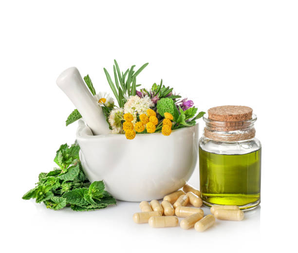 Medicinal herbs in mortar with pestle, organic essential aroma oil in glass bottle and pile of herbal capsules isolated on white background. Herbal medicine concept.